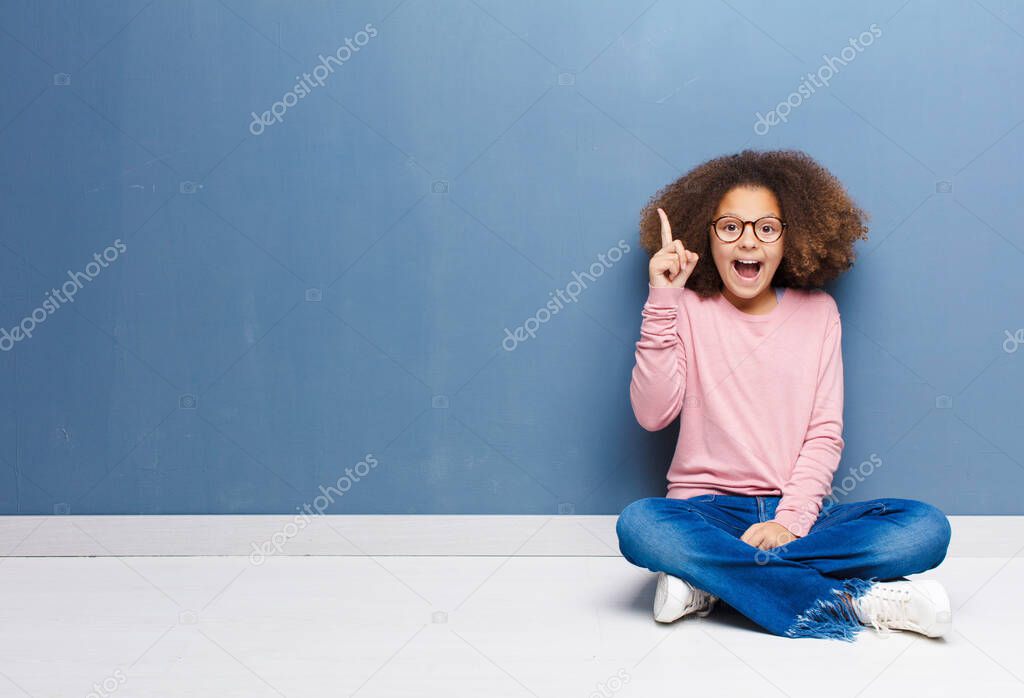 african american little girl feeling like a happy and excited genius after realizing an idea, cheerfully raising finger, eureka! sitting on the floor
