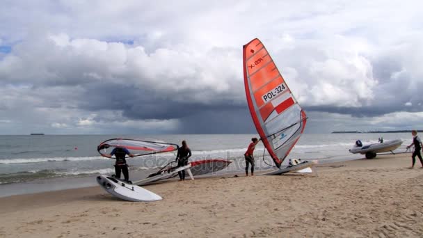 Lidé přinášejí prkna na windsurfing na břeh v Sopoty, Polsko. — Stock video