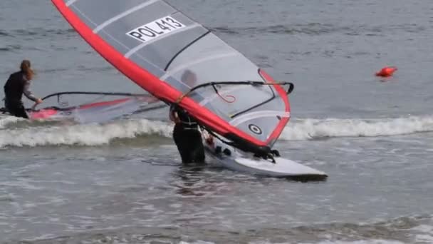 Lidé přinášejí prkna na windsurfing na břeh v Sopoty, Polsko. — Stock video