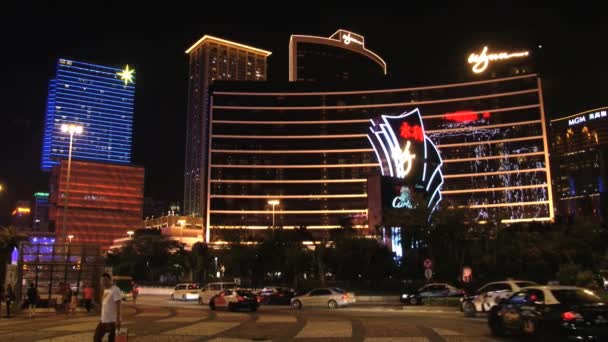 Mensen lopen door de straat met th Wynn hotel gebouw op de achtergrond bij nacht in Macau, China. — Stockvideo
