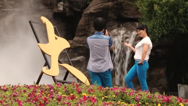 Chinese couple make travel photos with a smartphone in front of the waterfall in the Datang Furong Garden in Xian, China. — Stock Video