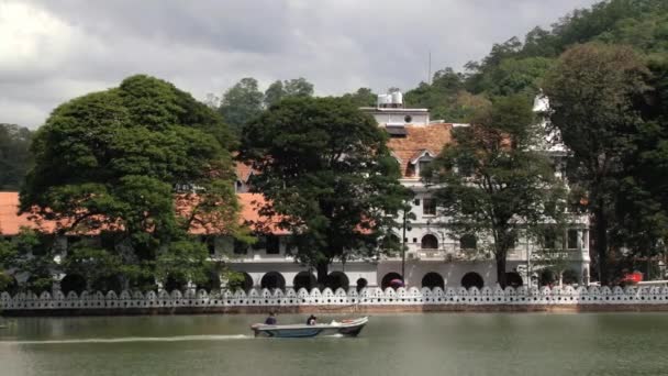 Mensen steken meer met de motorboot met de tempel van de tand (Sri Dalada Maligawa) op de achtergrond in Kandy, Sri Lanka. — Stockvideo