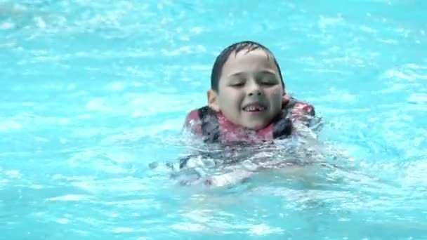 Chico con chaleco salvavidas hace un chapoteo con sus pies. Moción lenta en la piscina . — Vídeos de Stock