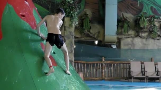 Мальчик веселится прыгая в аквапарке с водными горками . — стоковое видео