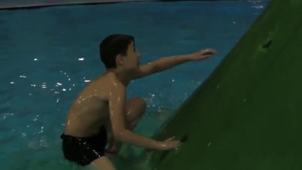 Garçon grimpant au sommet de la glissière d'eau dans le parc aquatique . — Video