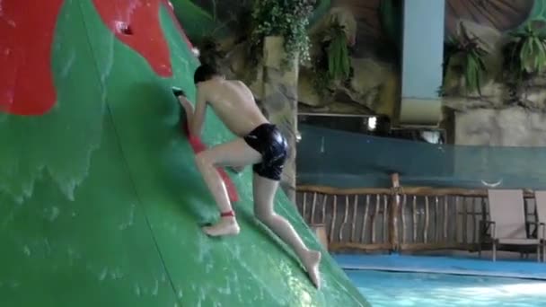 Ragazzo che si arrampica sulla cima dell'acquascivolo nel parco acquatico . — Video Stock