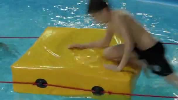 Развлечения для детей в бассейне. Коврик, на котором сидит мальчик . — стоковое видео