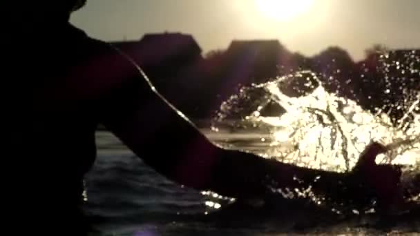 A mão da mulher faz respingo na água em câmera lenta durante o pôr do sol . — Vídeo de Stock