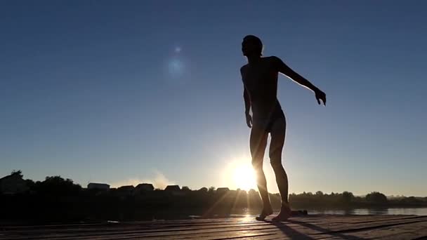 Mann auf der Brücke springt bei Sonnenuntergang in Zeitlupe in den Himmel. — Stockvideo