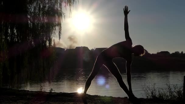 Sziluettjét az ember áll a jóga póz háromszög. A tó naplemente. — Stock videók