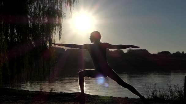 Silhouette des Mannes, der auf Yoga-Pose Krieger. Sonnenuntergang auf dem See.
