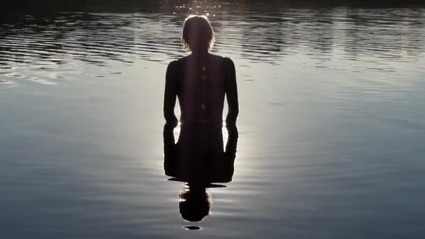 Un uomo sta nell'acqua e medita al tramonto . — Video Stock