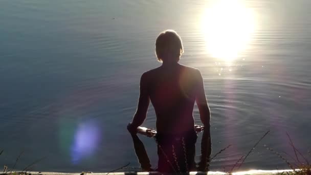 Un uomo sta nell'acqua e medita al tramonto . — Video Stock