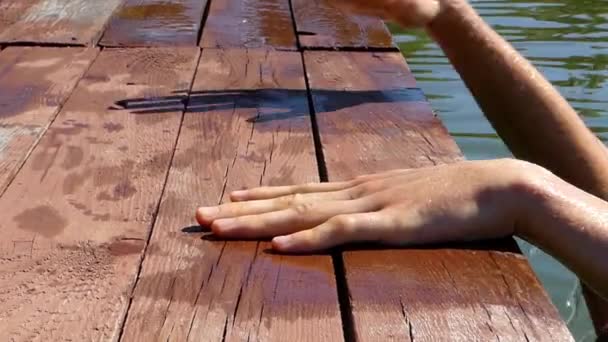 Ξανθιά ανεβαίνει έξω από το νερό σε μια ξύλινη γέφυρα. Τα χέρια, κοντινό πλάνο. — Αρχείο Βίντεο