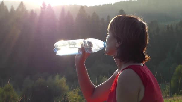 Silueta de mujer que bebe agua en las montañas al atardecer . — Vídeo de stock