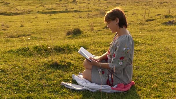 Kvinnan läser boken och ler mot solen lyser. — Stockvideo