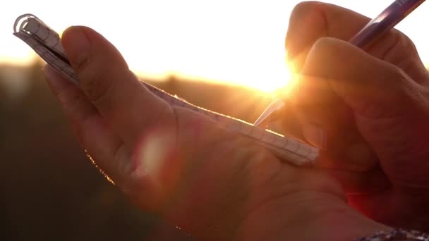 Flickans Hand att göra anteckningar i en anteckningsbok i solnedgången i solens strålar. — Stockvideo