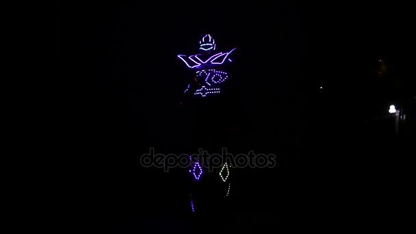 Un payaso con el traje de luz led en los zancos bailando por la noche . — Vídeo de stock