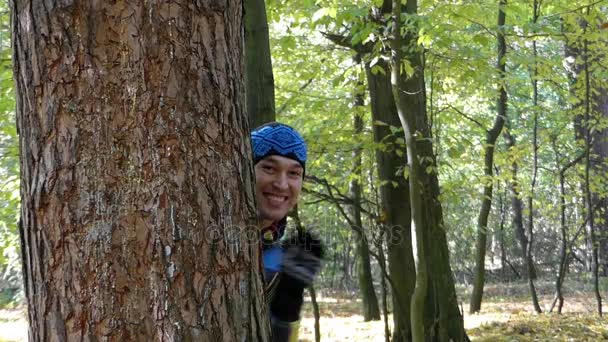 Um homem engraçado espreitando e enviando beijo de ar de trás de uma árvore de pinheiro . — Vídeo de Stock
