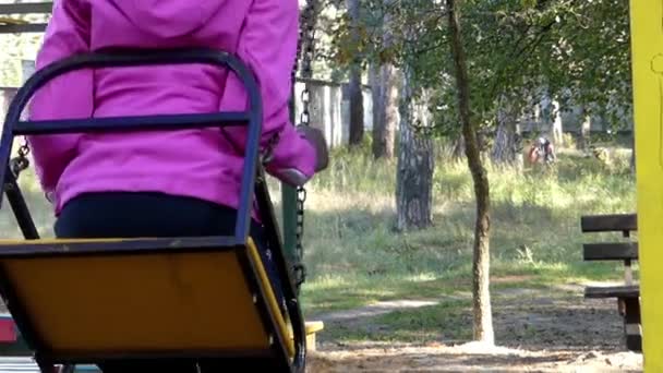 Uma menina entretendo em um balanço de corrente em um parque infantil no outono . — Vídeo de Stock