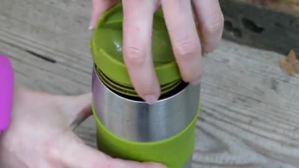 Une main de fille ouvrant un thermos en acier inoxydable avec de l'eau dans une forêt . — Video