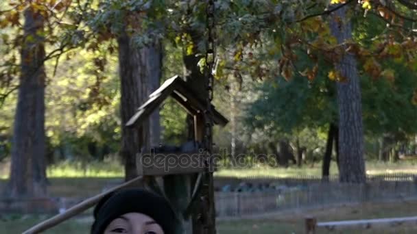 Een jonge vrouw swingen met een voeding Birdhouse op de achtergrond in Slow Motion. — Stockvideo