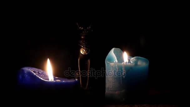 Due candele blu scuro e una statuetta di gatto nero egiziano tra di loro di notte . — Video Stock