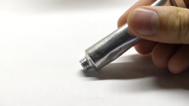 Uma mão espremendo para fora uma mancha de tinta de cor preta em uma folha branca de papel . — Vídeo de Stock