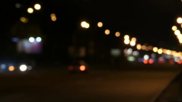 Ένα λεωφορείο και ένα αυτοκίνητο κινείται αργά Δειπνήστε ένα δρόμο της πόλης το βράδυ σε μια Defocused βολή. — Αρχείο Βίντεο