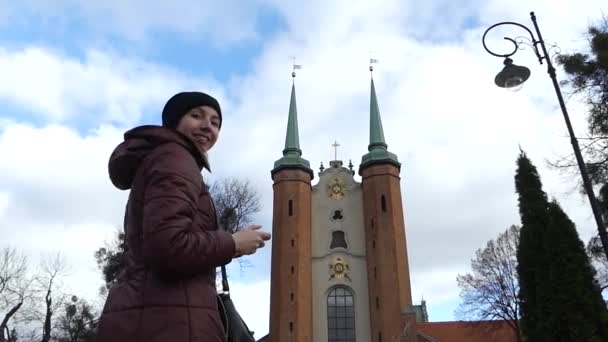 Duas torres góticas católicas com altos campanários e um relógio entre eles sendo baleado por uma bela garota europeia — Vídeo de Stock
