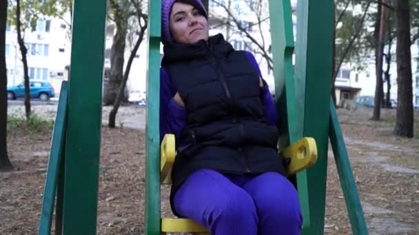 A Young Romantic Woman Sitting on a Moving Wooden Swing With Hands in Pockets. — Stock Video