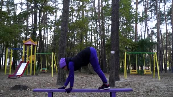 Una joven hermosa y enérgica haciendo un yoga asana con la cabeza hacia abajo en un banco . — Vídeos de Stock