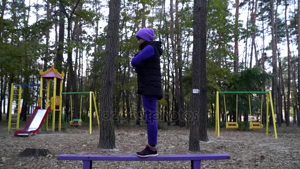 Eine attraktive junge Frau bei einer beeindruckenden Yoga-Übung hebt Bein und Arm auf dem Waldspielplatz. — Stockvideo