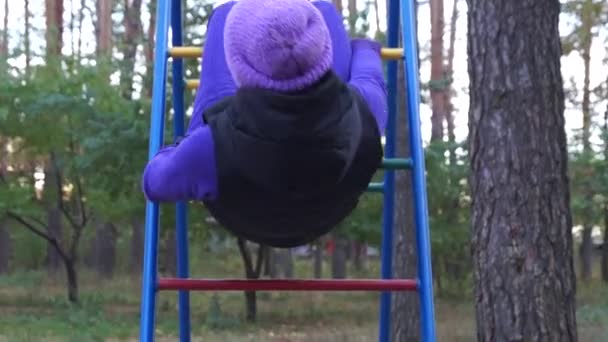 Een lachende jonge vrouw hangt op knieën op de Ladder van een speeltuin en doen Yoga oefening in de herfst — Stockvideo