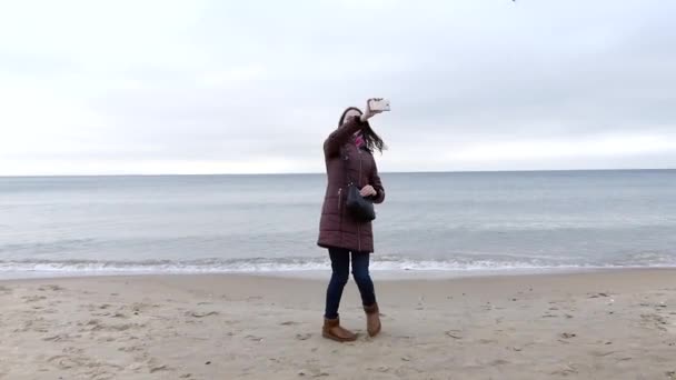 Una bella ragazza con lunghi capelli castani gira intorno mentre prende una foto selfie su una spiaggia di sabbia del mare in Slo-Mo — Video Stock