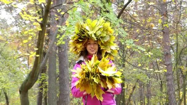 Красивая девушка с венком из листьев на голове, стоящая и улыбающаяся в лесу . — стоковое видео