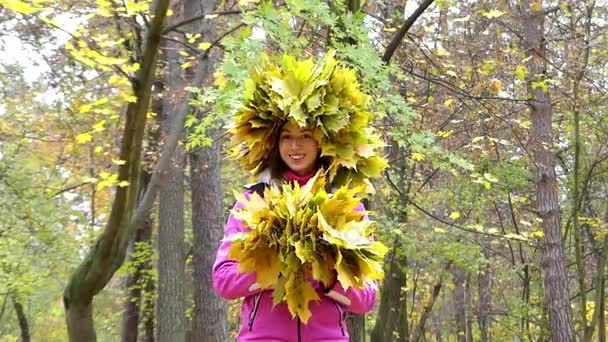 Щаслива дівчина з вінком листя на голову кидали жовтого листя в небо над головою. — стокове відео