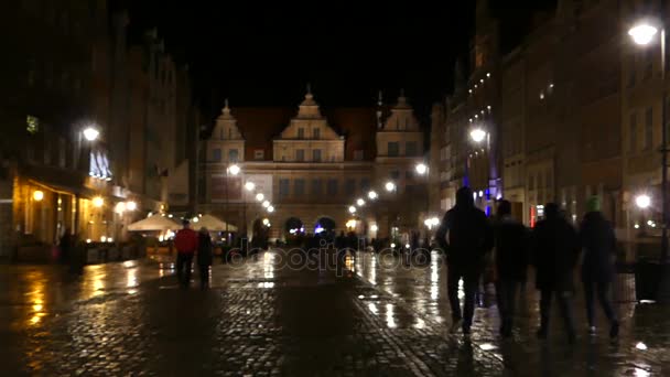 Un palacio amarillo europeo viejo bien iluminado y gente que camina a lo largo de una plaza de adoquines en la noche . — Vídeos de Stock