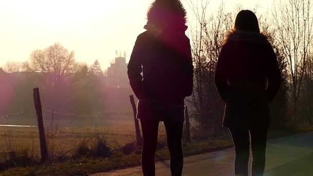 Два молодих дівчат, гуляючи по дорозі в сонячних променів ранкового сонця восени — стокове відео