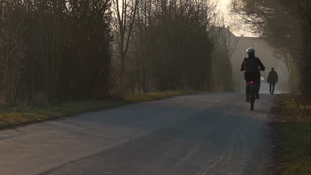 Un cycliste dans un casque fait du vélo le long d'une étroite route de village au ralenti . — Video
