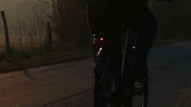 Ein junger männlicher Radfahrer, der auf einer Dorfstraße im Sonnenuntergang in Zeitlupe fährt. — Stockvideo