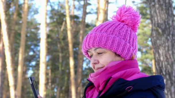 Mujer sonriente con sombrero rosa Respuesta en su tableta en el bosque en video de 4k . — Vídeos de Stock