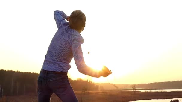 Энергетичный молодой человек с распростертыми объятиями танцует чертовски и поднимает руки на лавочке под открытым небом в медленном движении заката — стоковое видео