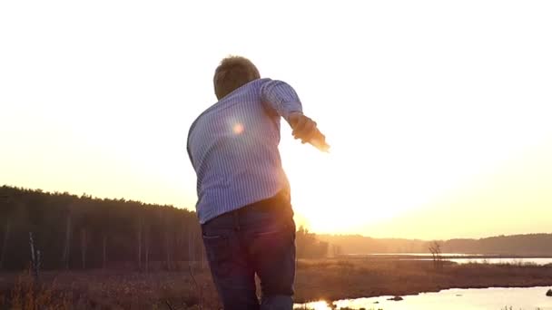 Energetic Young Man está bailando al aire libre mirando una puesta de sol, mientras está en un césped de algún campo a principios de primavera en cámara lenta — Vídeo de stock