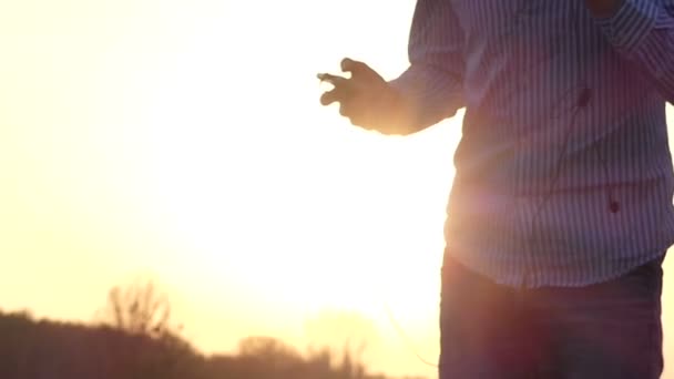 Le jeune homme se tient debout sur le terrain et regarde son Palyer avec un beau coucher de soleil Rayons dans le contexte au ralenti — Video