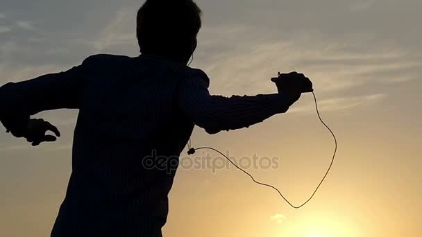 Energetic Young Man está bailando al aire libre mirando una puesta de sol, mientras está en un césped de algún campo en cámara lenta . — Vídeos de Stock