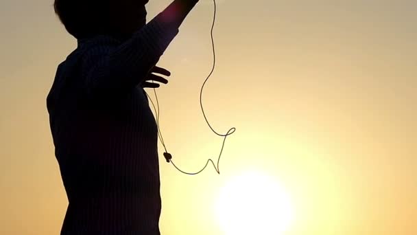 Young Man is Raising His Hands and Dancing With Earbuds in Ears and a Player in Hands With the Sunny Rays Beaming From Behind in Slow Motiom — Stock Video