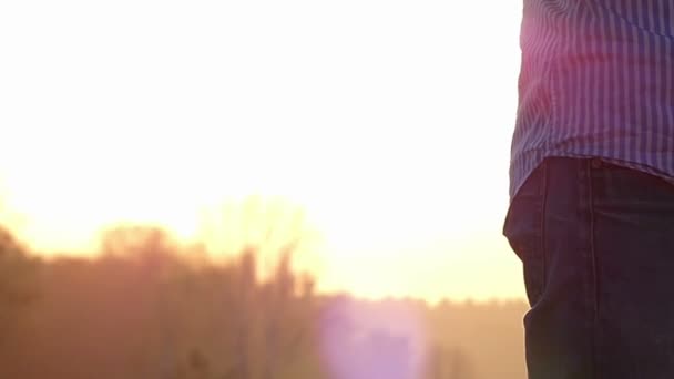 Jovem está de pé no campo e olhando para o seu palyer com um belo pôr do sol Raios no Backgroung em câmera lenta — Vídeo de Stock