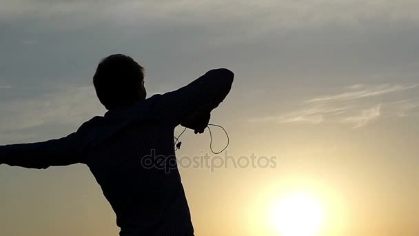 Jovem está dançando com fones de ouvido em mãos ao pôr do sol em câmera lenta . — Vídeo de Stock