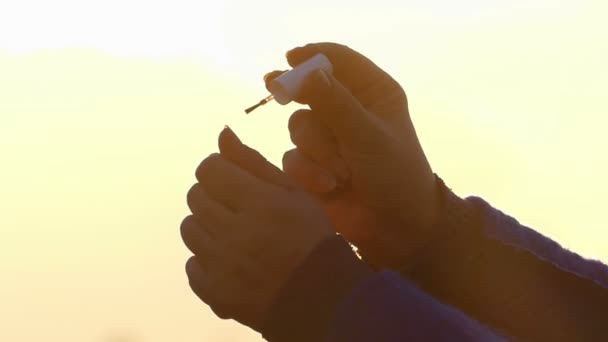 Handen van een vrouw die betrekking heeft op haar nagels met make-up Pools op de zonsondergang in het vroege voorjaar — Stockvideo